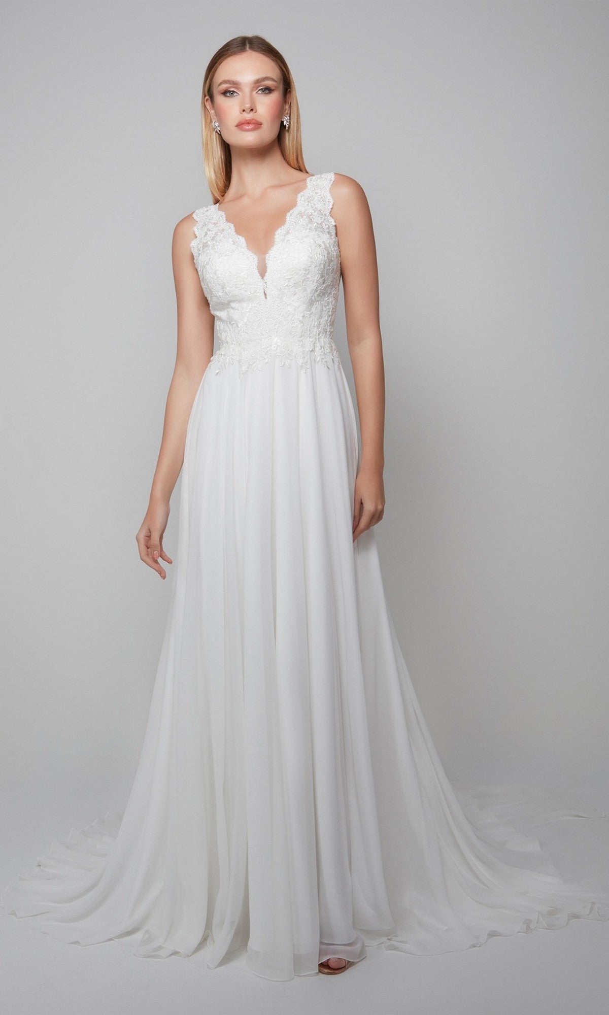 A woman in the Long White Dress: Alyce 7071, featuring lace on the bodice and a flowing ivory chiffon skirt, stands against a plain light gray background.